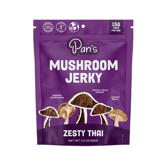 Pan's Mushroom Jerky Thai Mushroom Snack Foods with zesty flavor, dried mushroom slices on a rustic wooden surface.