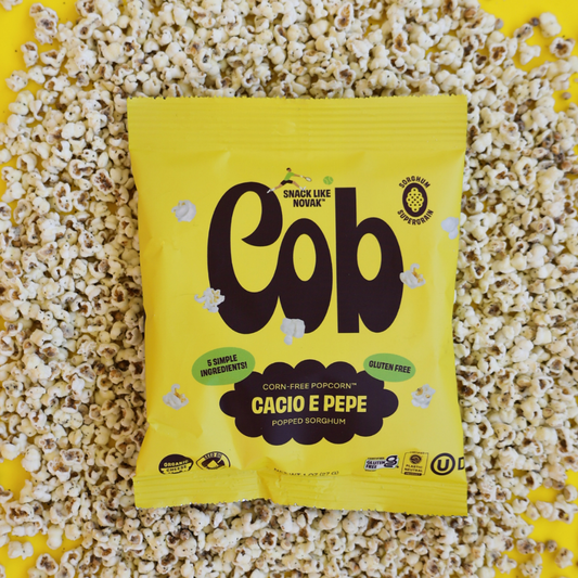 Cob Foods Cacio E Pepe Popped Sorghum in a bowl with crunchy, golden popped snack pieces displaying cheese and pepper seasoning.