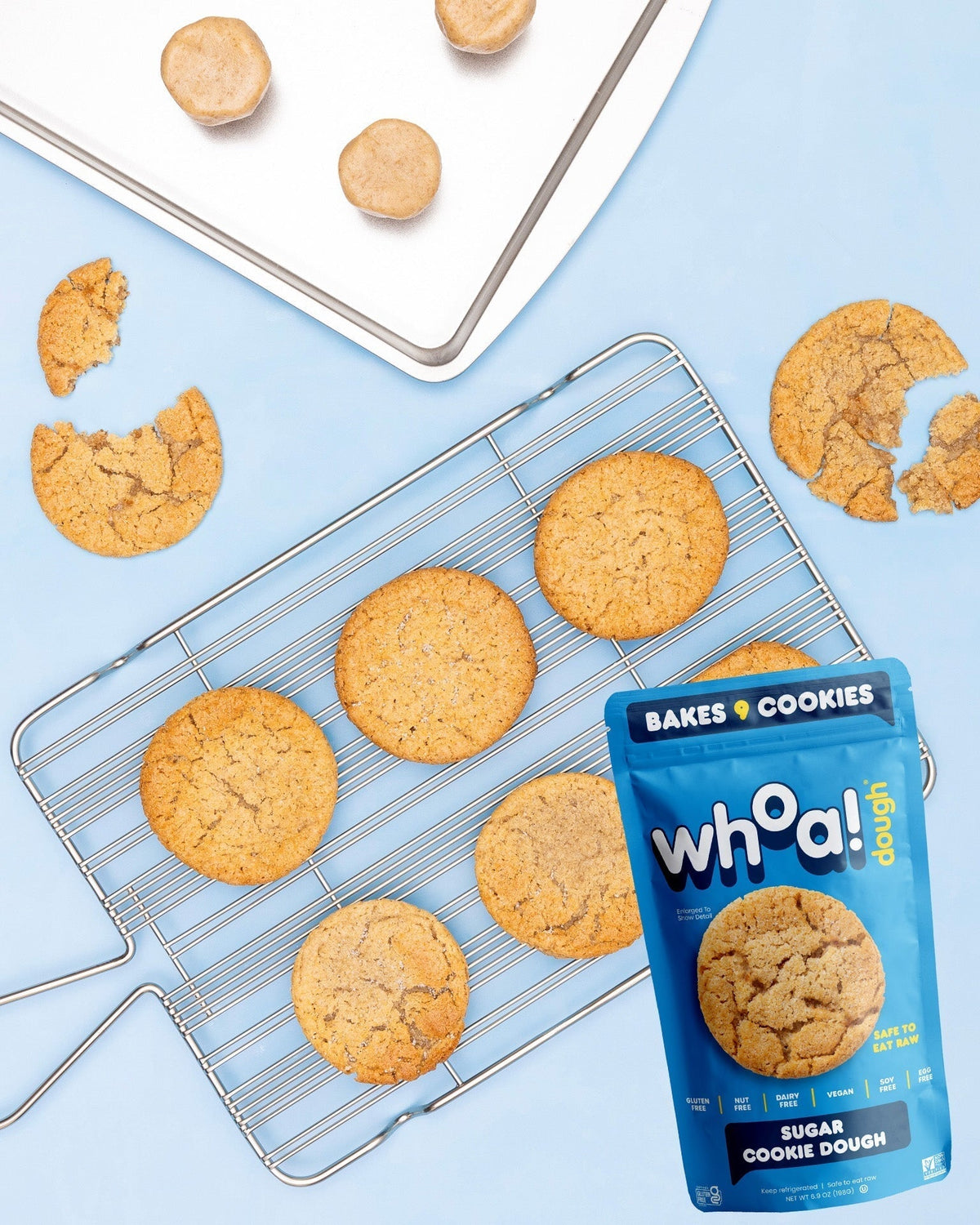 Whoa Dough Ready to Bake Sugar Cookie dough ball on baking sheet, ready for baking, with cookie cutter shapes on a white surface.