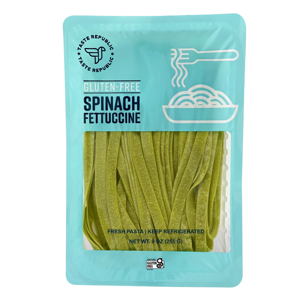 Fresh gluten-free spinach fettuccine pasta from Taste Republic Gluten-Free, displayed in a 6-pack with uncooked pasta on a white surface.