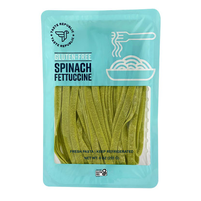 Fresh gluten-free spinach fettuccine pasta from Taste Republic Gluten-Free, displayed in a 6-pack with uncooked pasta on a white surface.