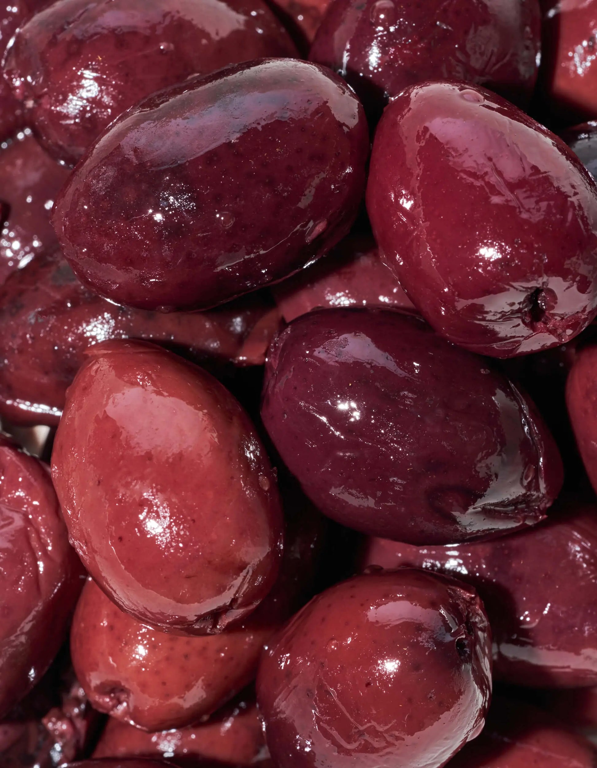 Fresh Kalamata olives in extra virgin olive oil from FreeStyle Snacks, displayed in a clear glass bowl on a neutral background.