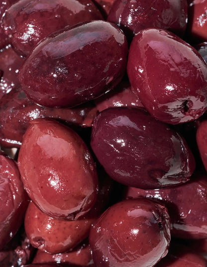 Fresh Kalamata olives in extra virgin olive oil from FreeStyle Snacks, displayed in a clear glass bowl on a neutral background.