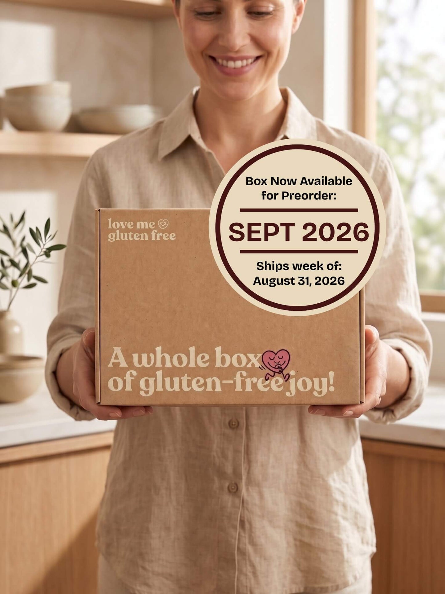 A smiling woman in a beige linen shirt holds a brown cardboard box labeled 'love me gluten free' and 'A whole box of gluten-free joy!' in a softly lit kitchen. A large circular badge on the box says the box is now available for preorder in Sept 2026 and ships week of August 31, 2026.