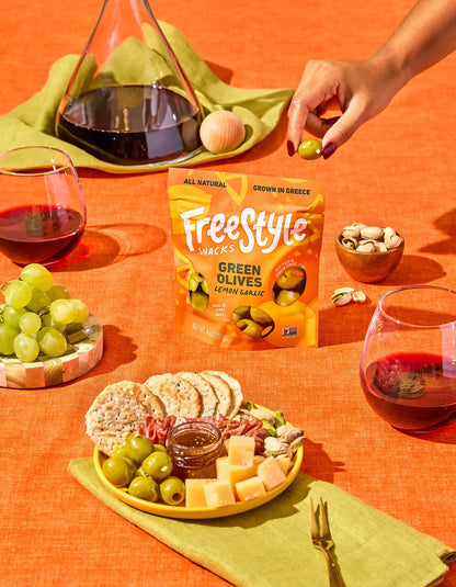 Fresh green olives with lemon and garlic from FreeStyle Snacks, displayed in a clear bowl on a rustic wooden table.
