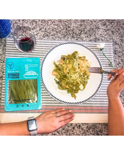 Fresh Taste Republic gluten-free spinach fettuccine pasta in a 6-pack, shown on a wooden surface with a fork and greenery.