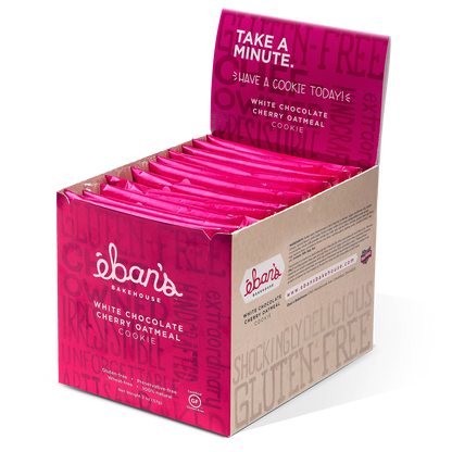 Open packaging of Eban's Bakehouse white chocolate cherry oatmeal cookies, showing golden cookies with white chocolate and cherry pieces.