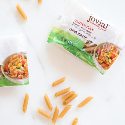 Single serving of Jovial gluten-free brown rice penne pasta on a white surface, showcasing the pasta's texture and shape.