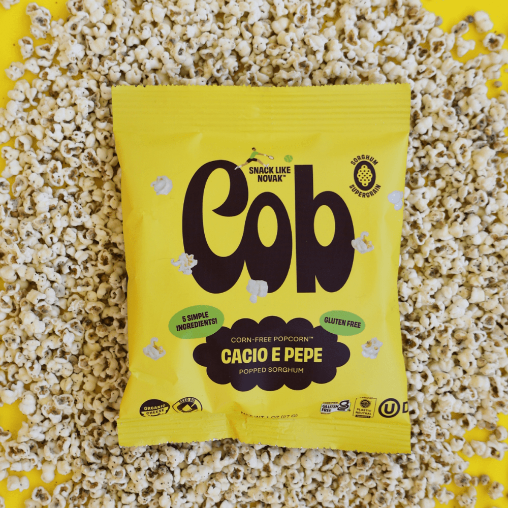 Cob Foods Cacio E Pepe Popped Sorghum in a bowl with crunchy, golden popped snack pieces displaying cheese and pepper seasoning.