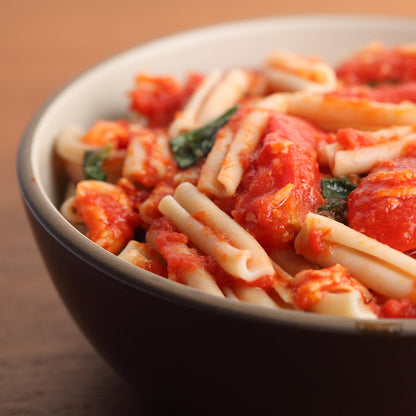 Gluten-free Jovial Brown Rice Caserecce pasta with garlic and tomato, served in a bowl with fresh herbs.