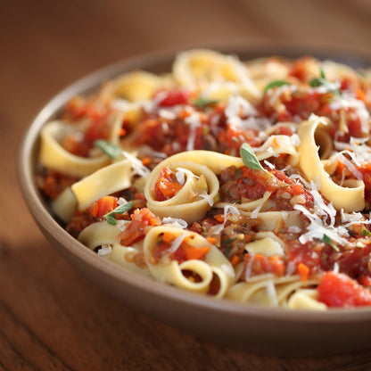 Gluten-free brown rice egg tagliatelle pasta by Jovial Foods, Inc, coiled on a white surface with some fresh herbs.