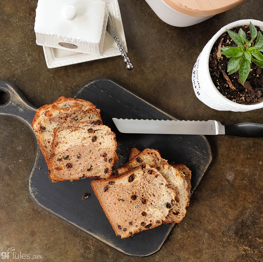 gfJules gluten-free cinnamon raisin bread loaf on a wooden board, showing golden crust and raisin-filled slices.