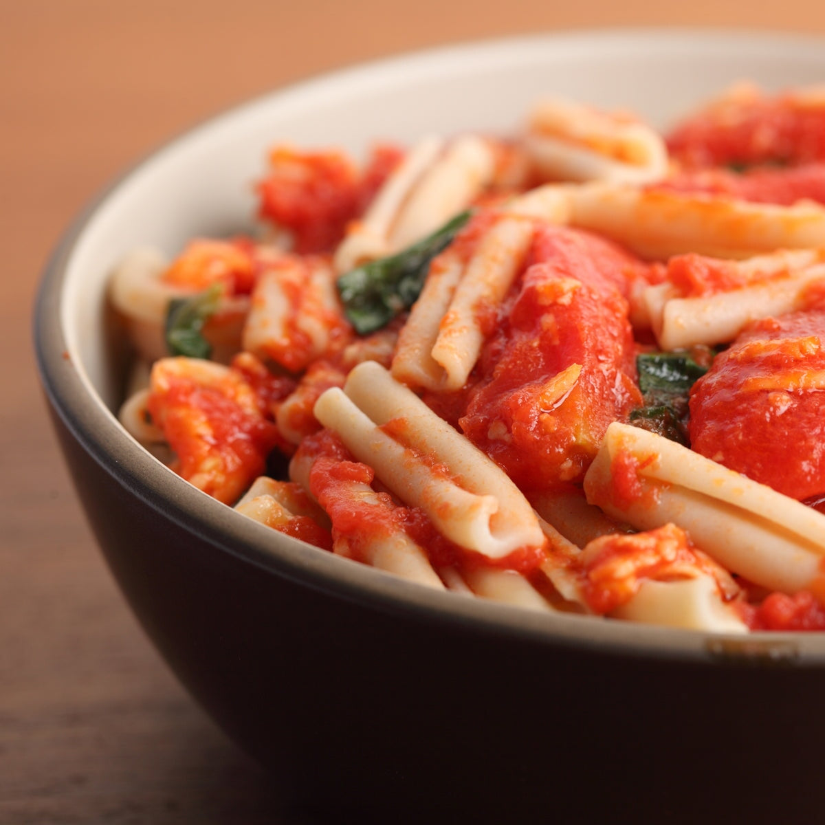Gluten-free Jovial Brown Rice Caserecce pasta with garlic and tomato, served in a bowl with fresh herbs.