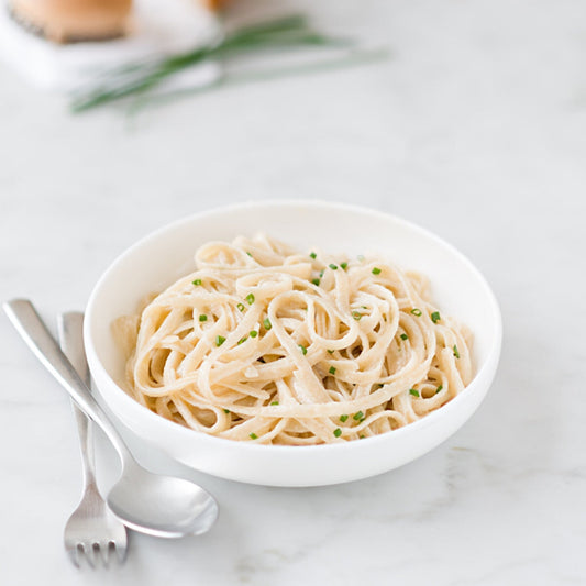 Gluten-free brown rice fettuccine pasta by Jovial Foods, Inc., cooked and served on a plate with fresh herbs and vegetables.