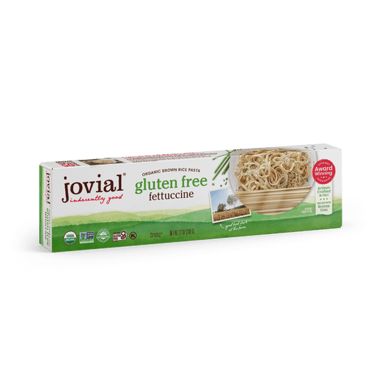 Jovial Gluten Free Brown Rice Fettuccine pasta, uncooked, showing long, flat noodles in a clear container with a white background.
