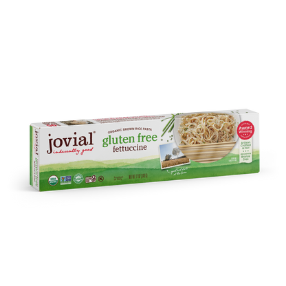 Jovial Gluten Free Brown Rice Fettuccine pasta, uncooked, showing long, flat noodles in a clear container with a white background.
