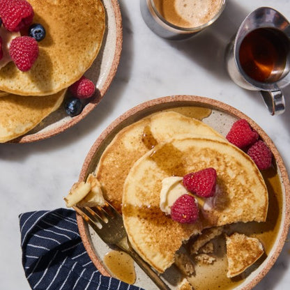 Gluten-free King Arthur Pancake Mix in a box, with a prepared stack of fluffy pancakes on a plate.