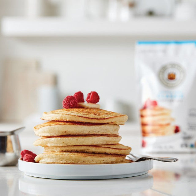 Stack of fluffy pancakes made with King Arthur Pancake Mix served on a white plate with butter and syrup.