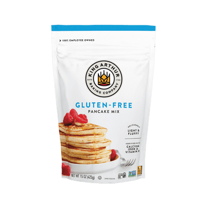 Box of King Arthur Pancake Mix with a scoop of prepared pancakes and syrup on a plate, showcasing the baking product and finished breakfast.