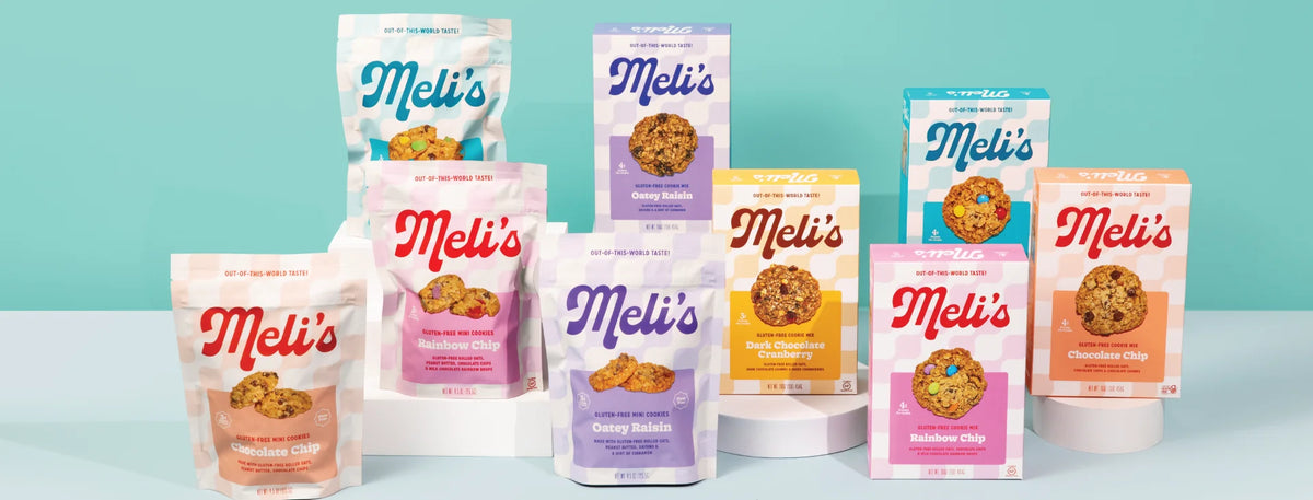A group of Meli's cookiesand boxes arranged on white display risers against a light teal background. The packaging features various colors including pink, orange, purple, yellow, and blue, with the brand name 'Meli's' prominently displayed on each package.