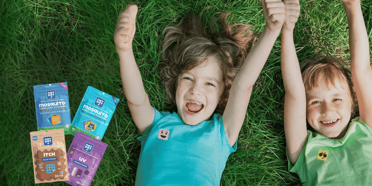 Two children lying on green grass with their arms raised, smiling and giving thumbs up, next to several colorful Morsky snack pouches.