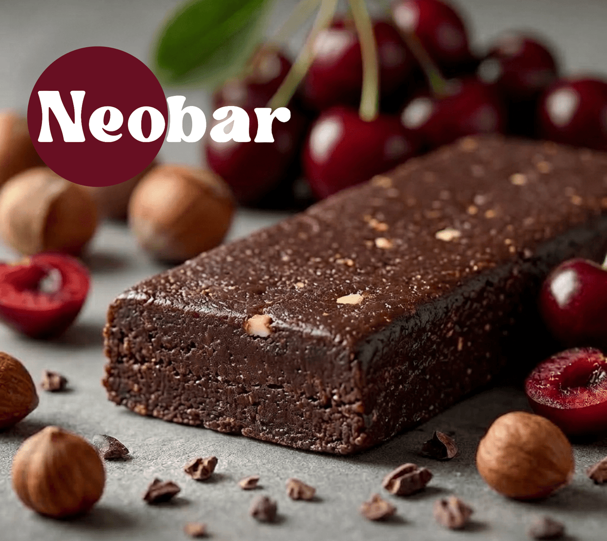 A dark chocolate bar with visible nuts and cherry pieces, styled on a gray surface with whole cherries, sliced cherries, and hazelnuts. A dark red circle in the upper left contains the white text 'Neobar'.
