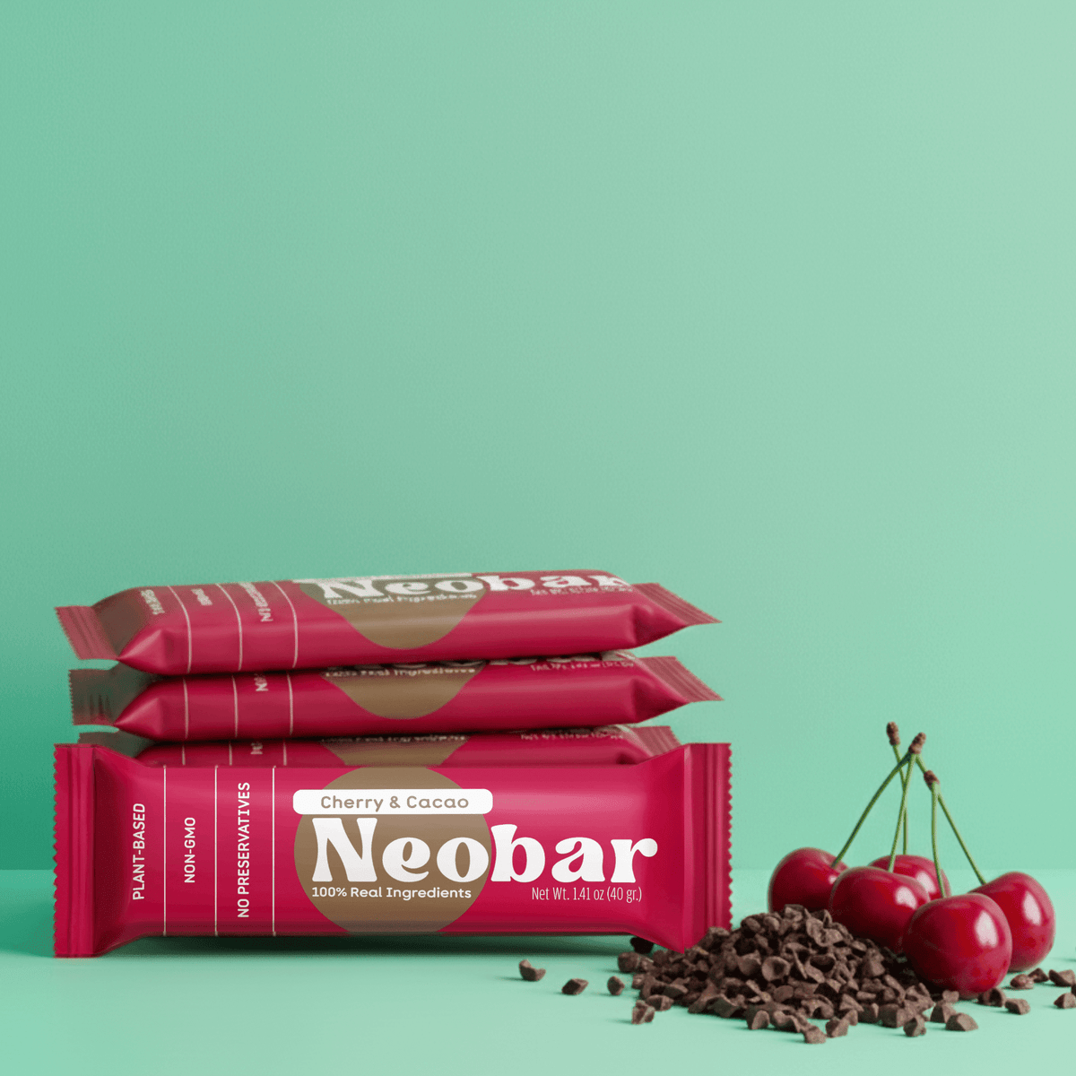 Three Neobar chocolate bars stacked on a mint green background, with red cherries and chocolate chips placed to the right. The packaging is bright pink with white and gold text.