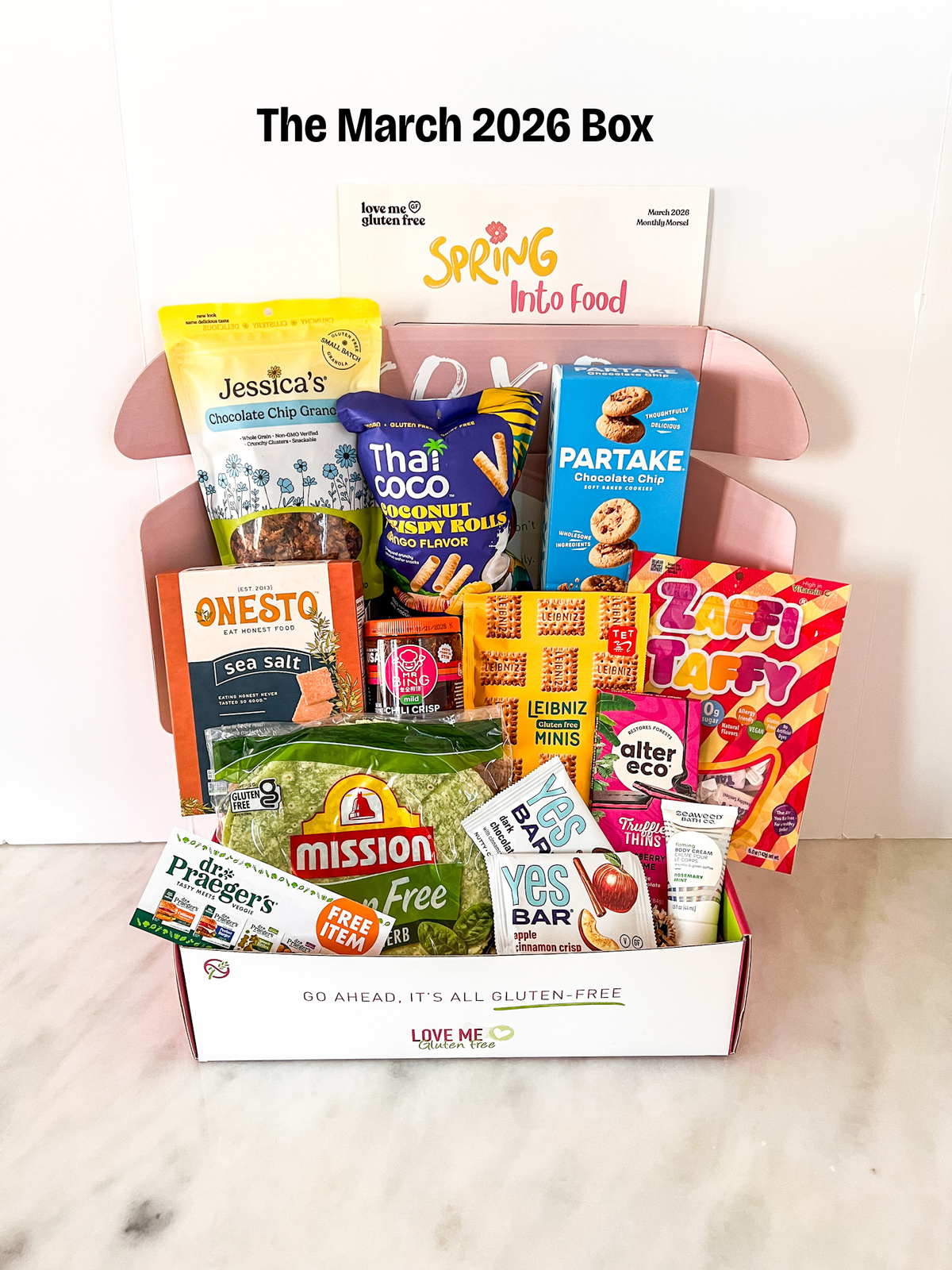Love Me Gluten Free March 2026 Box featuring assorted gluten-free snacks and treats in a decorative box.
